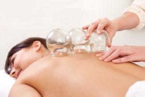 Acupuncture therapist removing a fire cupping glass from the back of a young woman