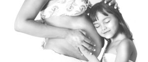 Pregnant mother and daughter leaning on her belly in black and white