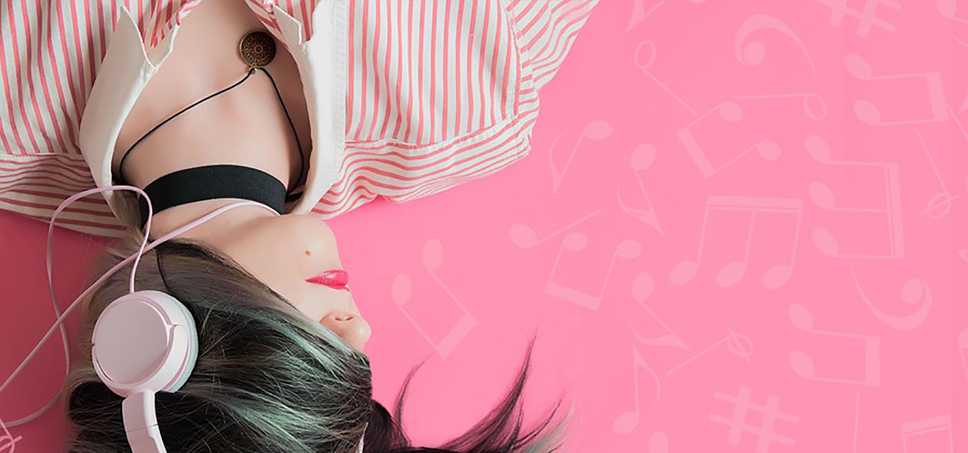 Woman with headphones lying down on a pink background.