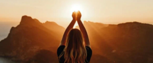 Woman with her hands up in the air covering the sunset