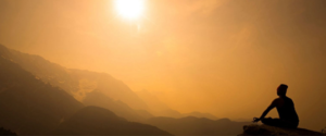 A silhouette of a person sitting on a mountain at sunset.