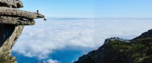 A man hanging off a cliff among blue skies and clouds.