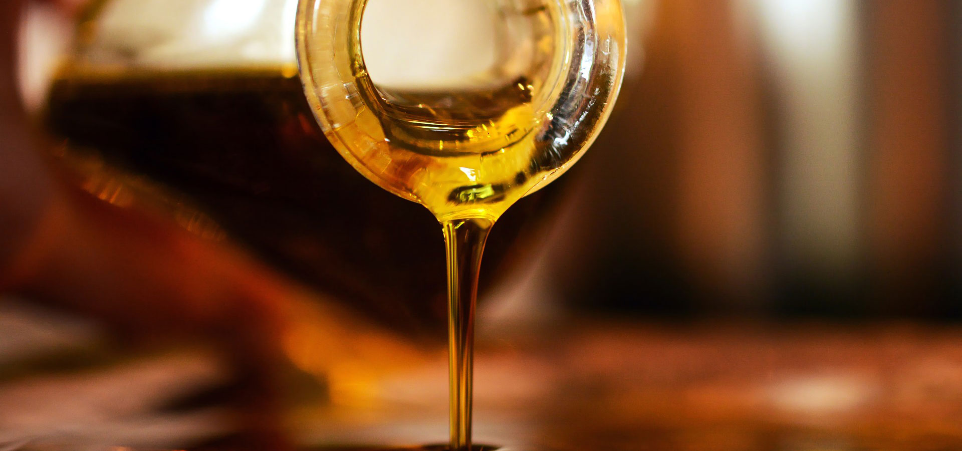 Close-up of golden liquid being poured from a glass container, symbolizing purity and natural ingredients, often associated with oils or honey.