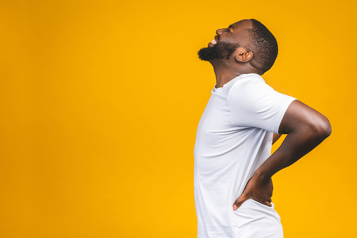 Man in a white shirt holding his lower back in discomfort representing back pain and the need for pain relief solutions.