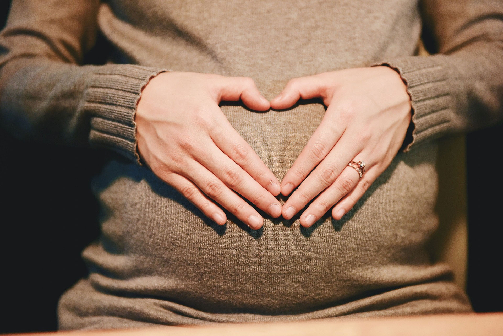 A pregnant belly with hands making a heart