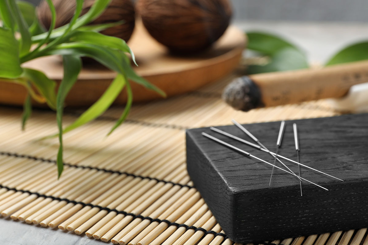 Acupuncture needles neatly placed on a black stone, surrounded by bamboo mat and natural elements, symbolizing traditional Chinese medicine and holistic healing.