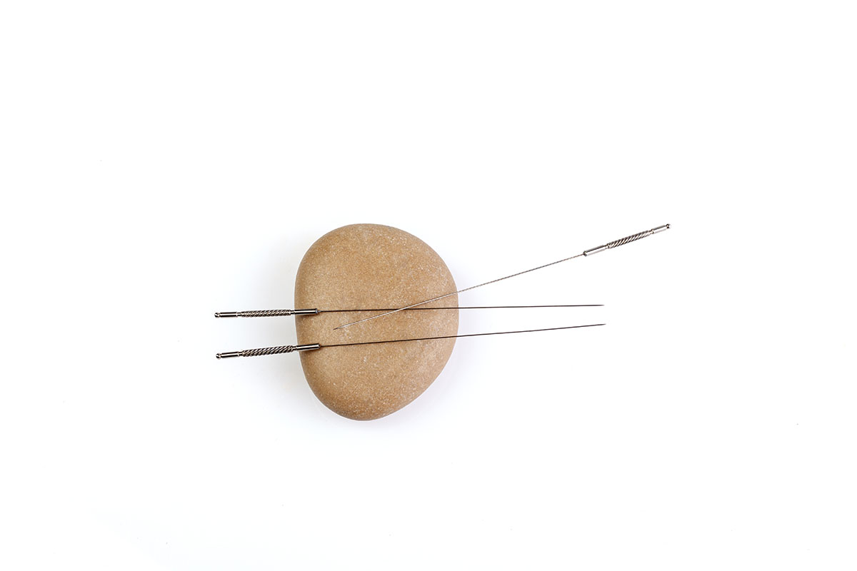 Three acupuncture needles resting on a smooth stone against a white background, symbolizing traditional Chinese medicine and holistic healing practices.