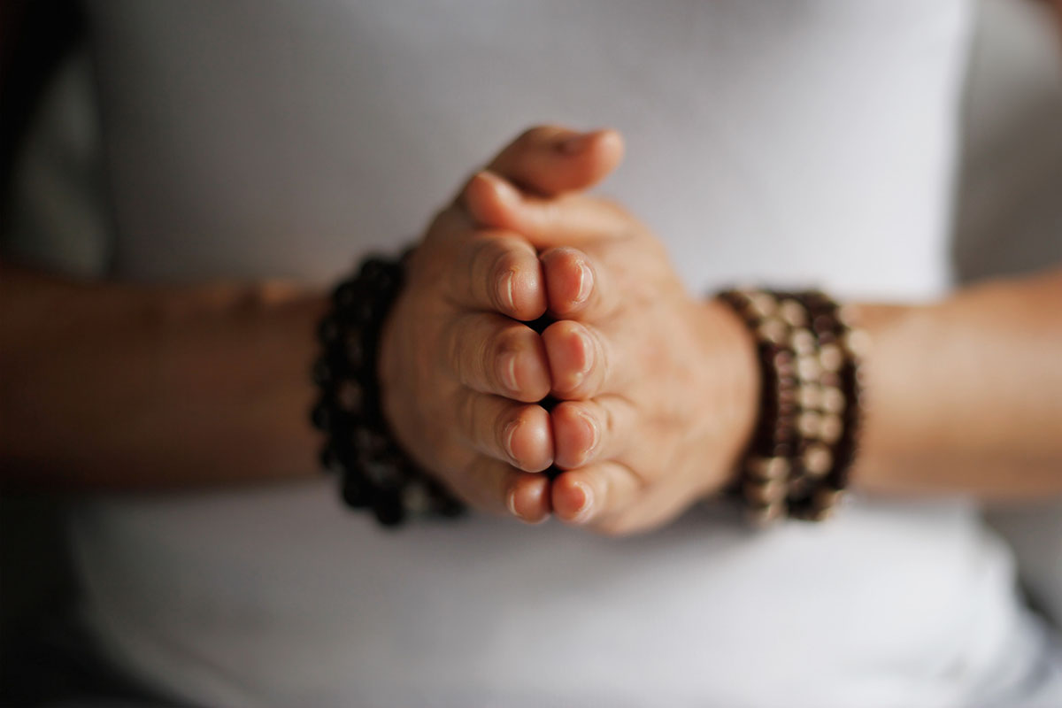 Close-up of hands in a prayer position with wooden bead bracelets, symbolizing mindfulness, meditation, and spiritual focus.