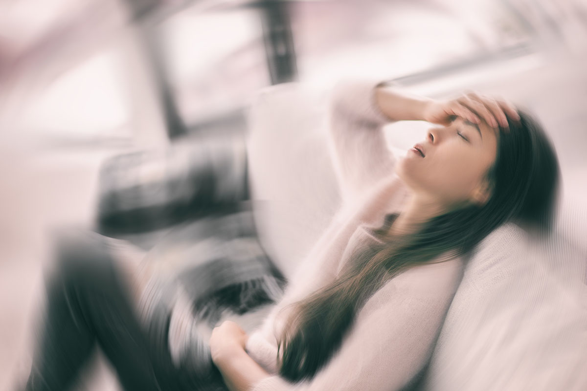 Blurred image of a woman experiencing dizziness and holding her head, illustrating symptoms of vertigo or migraines.