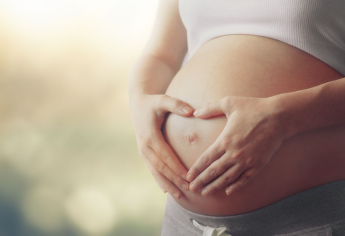 Pregnant woman's belly with fingers heart symbol.