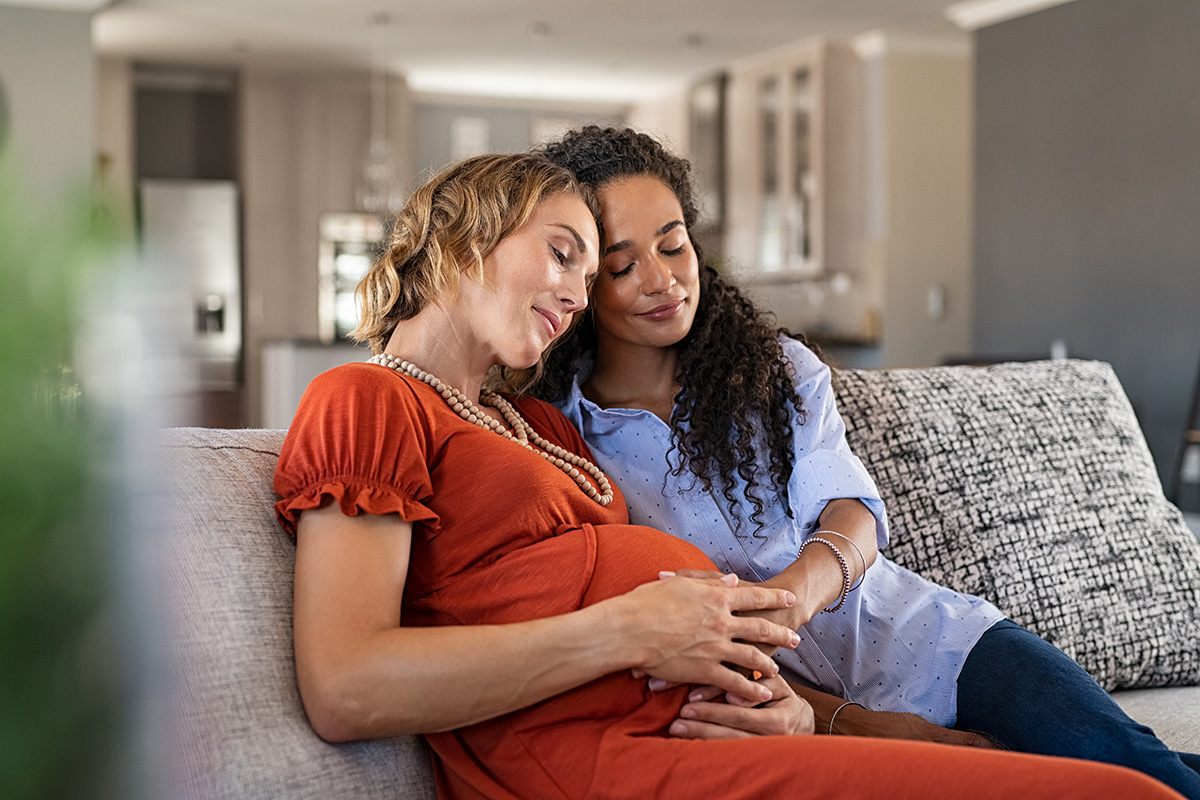 Couple with hands on baby bump of pregnant woman relaxing with eyes closed at home.