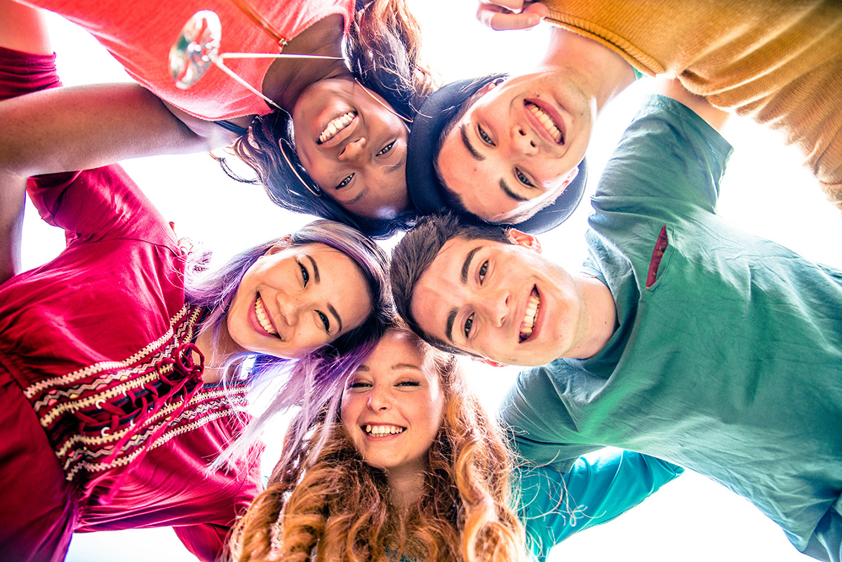 Group of diverse young friends smiling while huddled together outdoors, expressing happiness and unity.