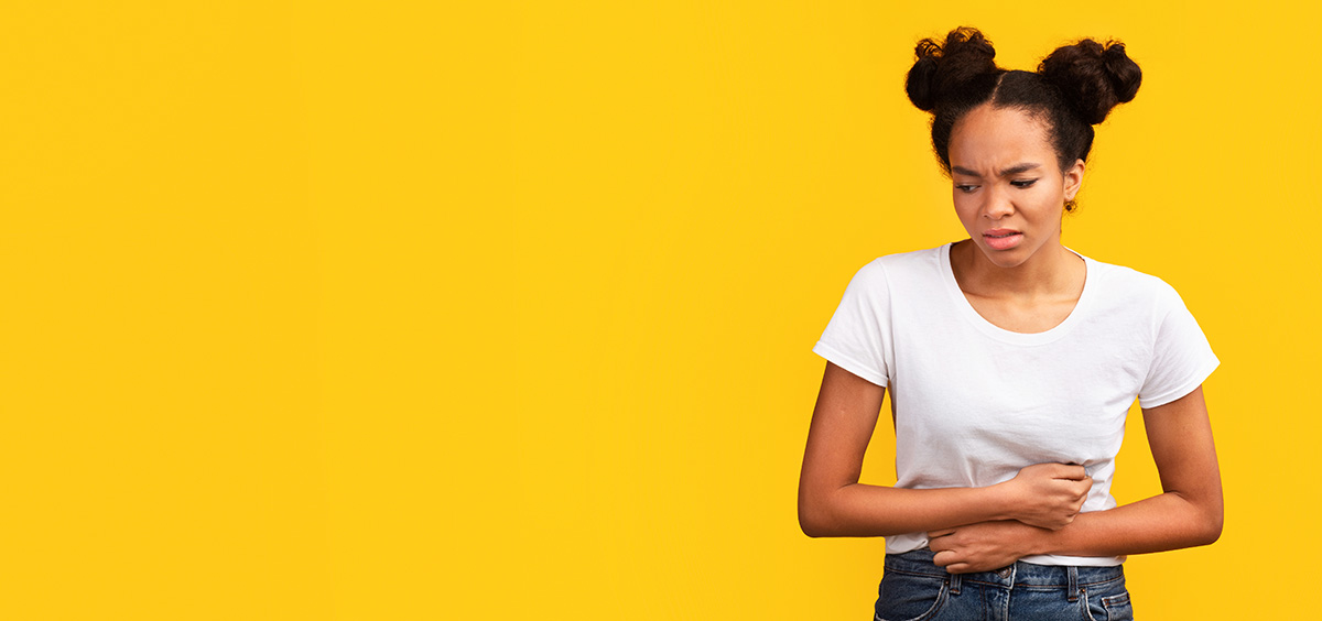 Young woman with a pained expression holding her stomach against a bright yellow background, representing discomfort from menstrual cramps.