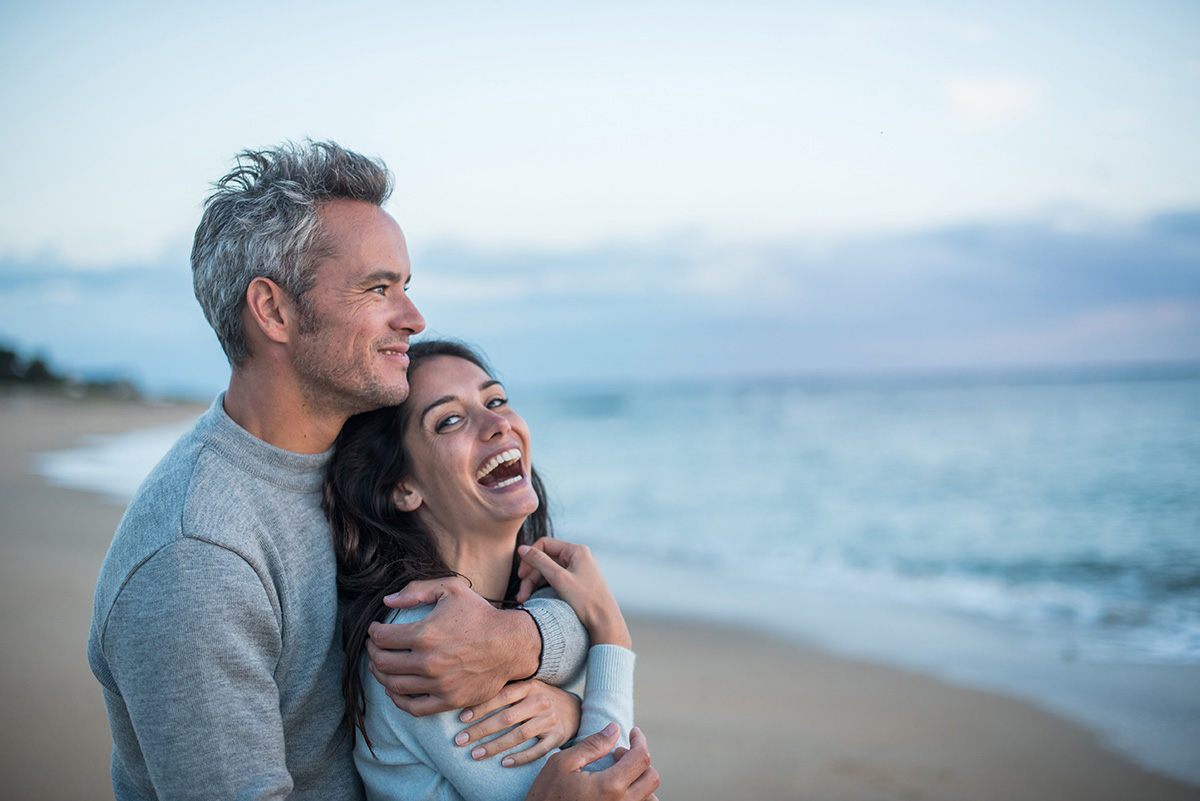 Beautiful couple on the beach at sunset. The man tightens the woman in his arms and they look at the horizon