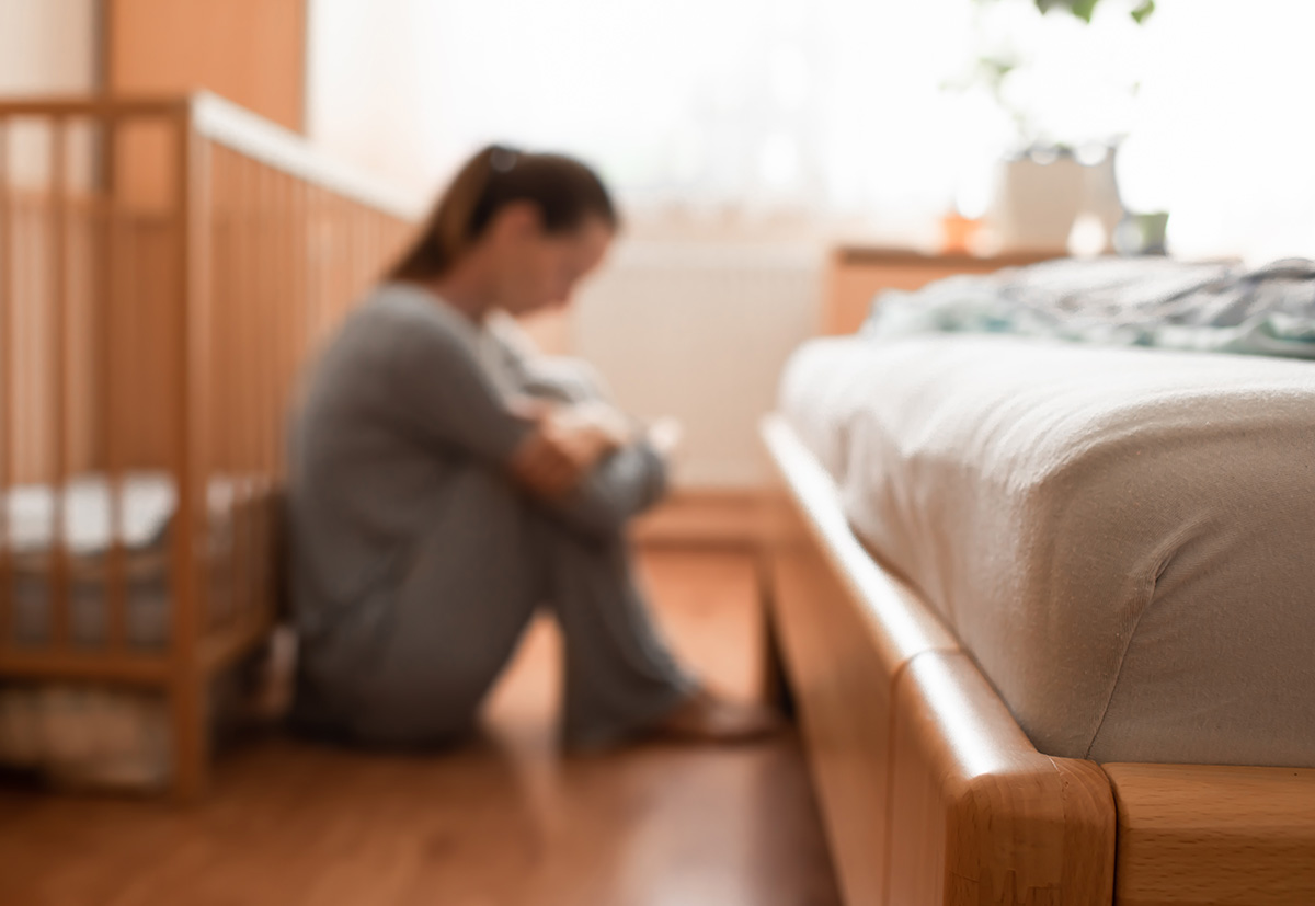 Blurred image of a distressed mother sitting on the floor beside a crib, symbolizing postpartum depression or emotional challenges of new motherhood.