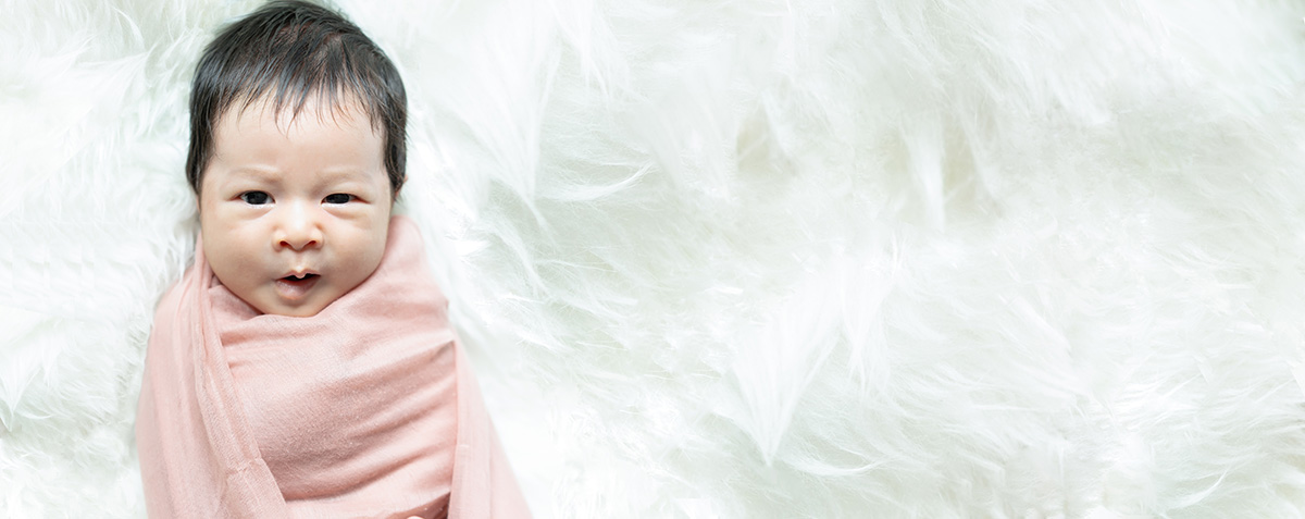 Adorable newborn baby wrapped in a soft pink blanket, lying on a fluffy white background, representing warmth and tenderness.