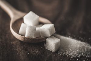 Close up sugar cubes and cane in wooden spoon on the table.