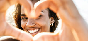 Close up image of smiling woman in swimwear on the beach making a heart shape with hands. Healthy lifestyle, self love and body care concept.