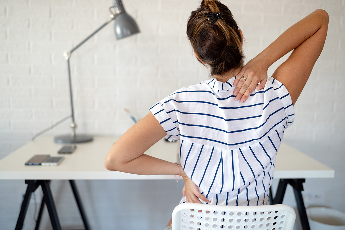 Overworked woman with back pain in office sitting on chair.