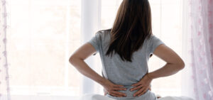 Sad young woman sitting on a bed suffering from back pain.
