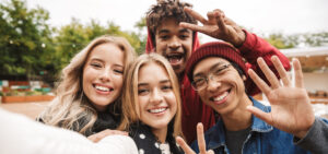 Group if cheerful teenagers spending fun time together outdoors, taking a selfie.