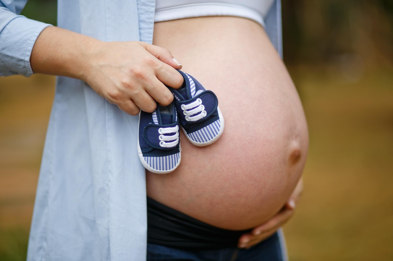 A soon to be Mom with a pregnant belly holding baby shoes
