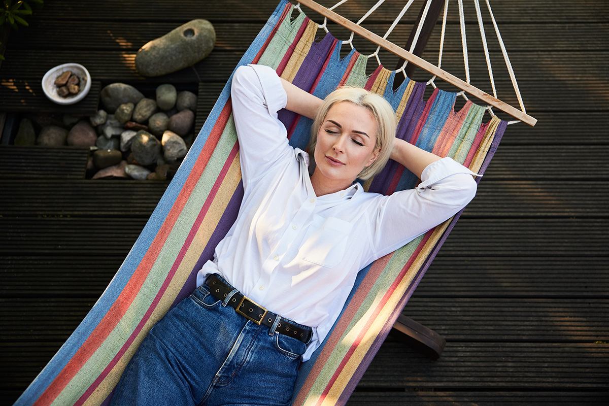 Adult woman sleeping in hammock on deck terrace during sunny summer afternoon. 