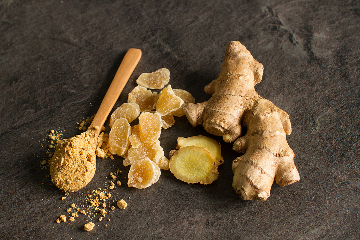 Ginger root, candied and ginger powder in wooden spoon over grey