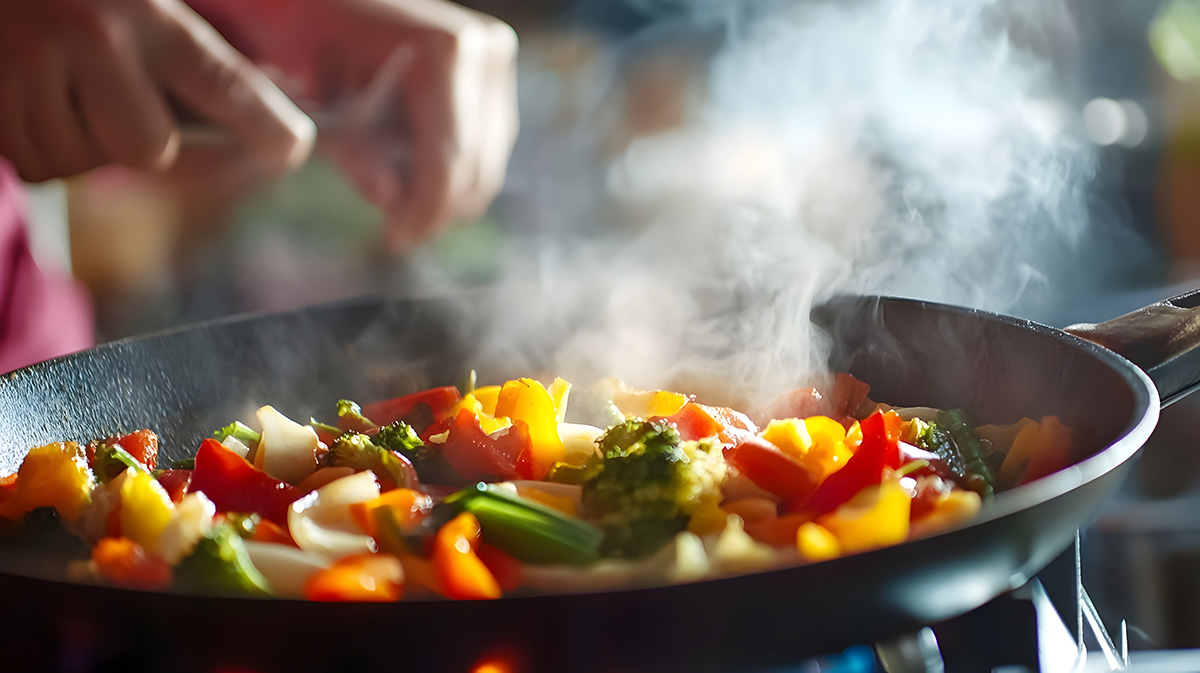 A vibrant pan filled with sauteed vegetables cooking on a stovetop, releasing steam and delicious aromas.