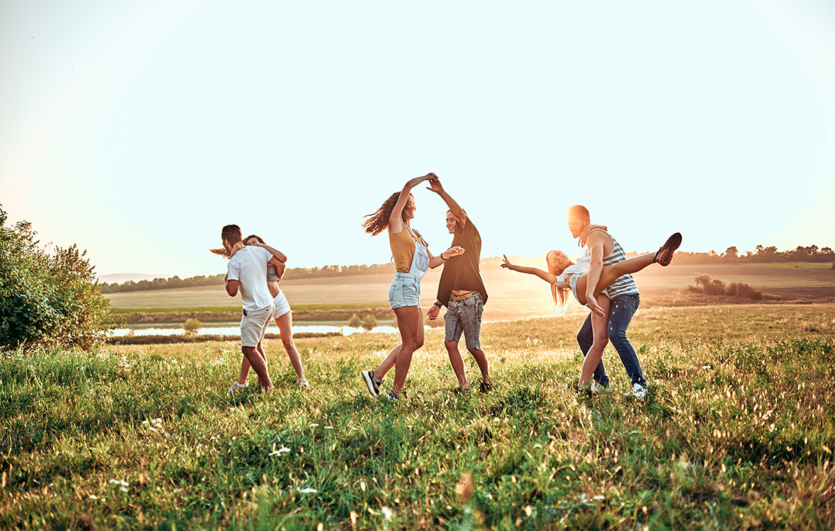 Group of happy young people dancing on the field on beautiful summer sunset.