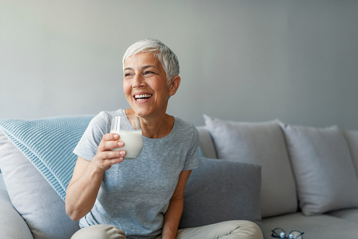 Happy senior woman having fun while drinking milk at home.