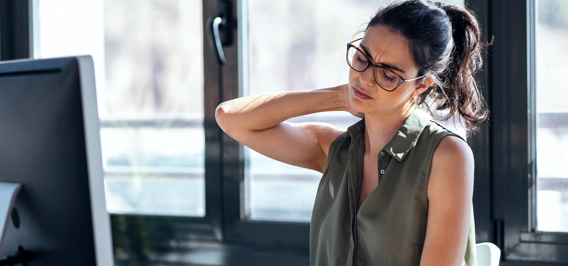 Tired business woman with neck pain looking uncomfortable while working with computer in the office.