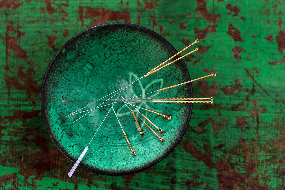 Green ceramic Asian Bowl with needles for acupuncture on an old green paint wooden board