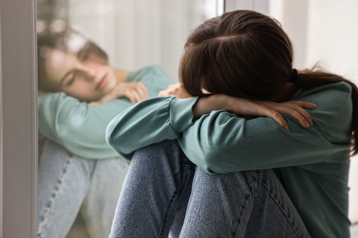Sad teenage girl near window at home