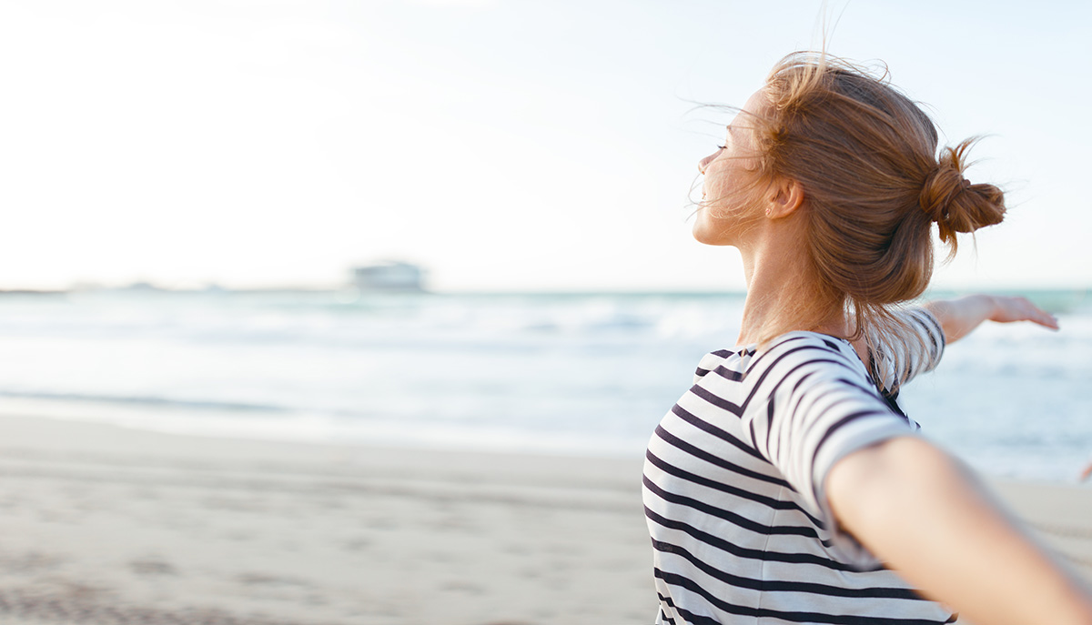 Happy young woman enjoying freedom with open hands on sea