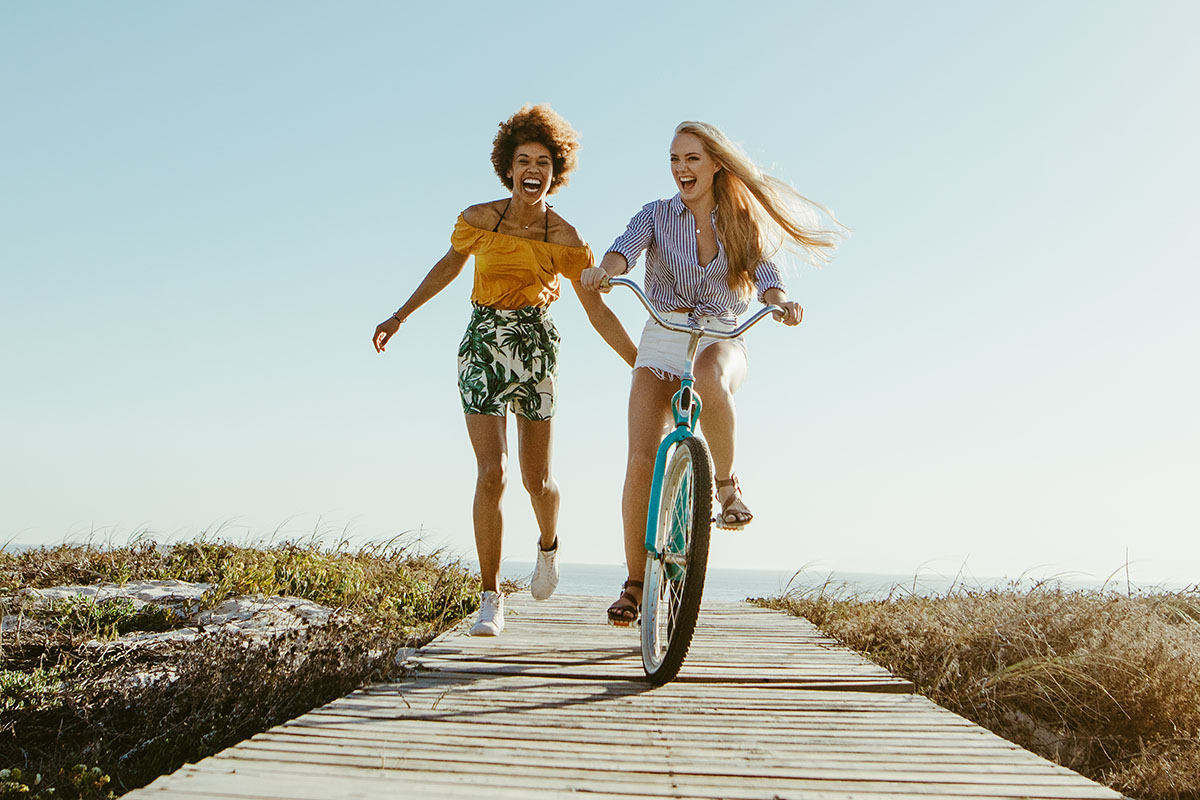 Excited woman riding bike down the boardwalk with her friends running along.
