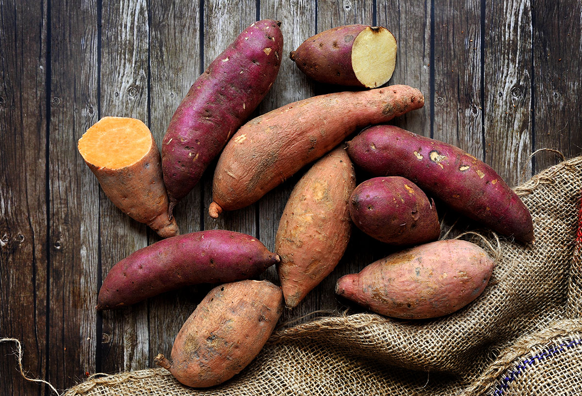 Mix of sweet potatoes with sack over wooden background