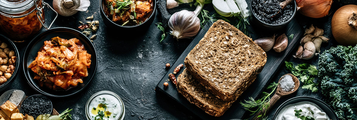 Probiotic foods such as kimchi, kefir, yogurt, and vegetables are displayed on a kitchen table