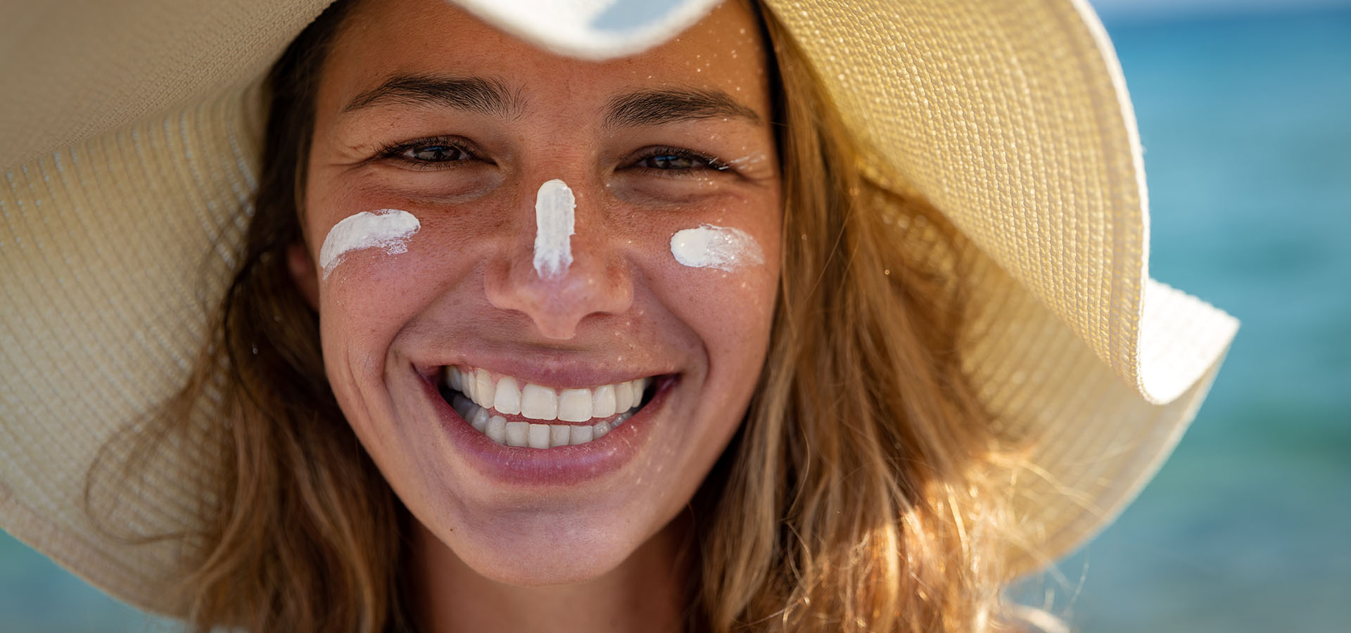 Close up of happy young smiling woman with straw hat and sunscreen on her face